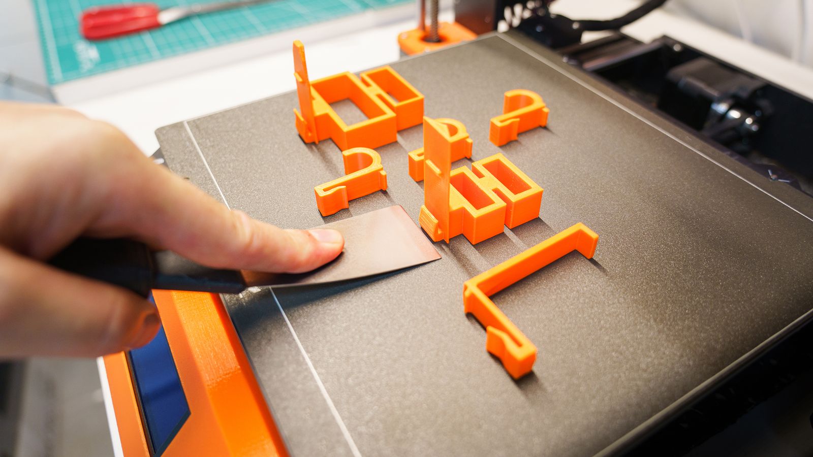 Mano retirando con una espátula una pieza impresa en 3D de la cama