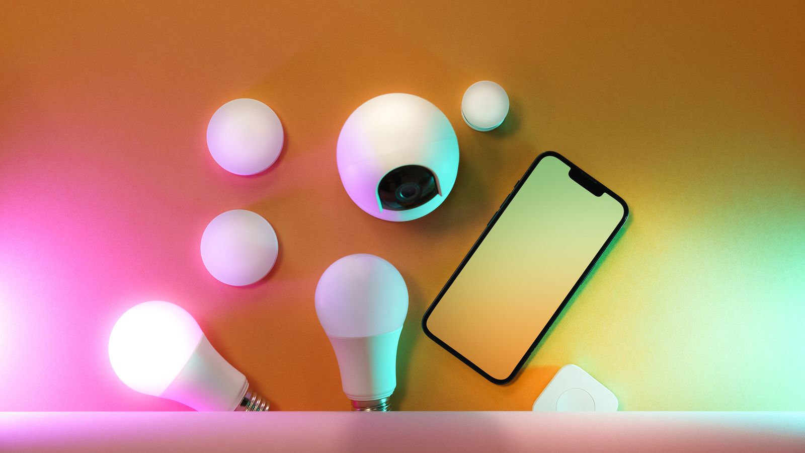 Varios dispositivos de hogar inteligente sobre una mesa: bombillas conectadas y un teléfono móvil
