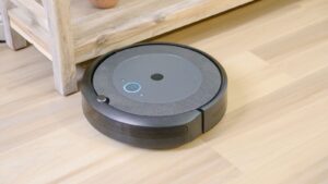 Robot aspirador limpiando un suelo de madera junto a una planta